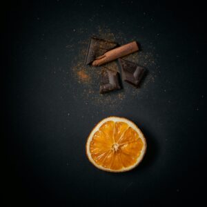 A stylish flat lay of sliced orange, chocolate, and cinnamon sticks on a dark surface.