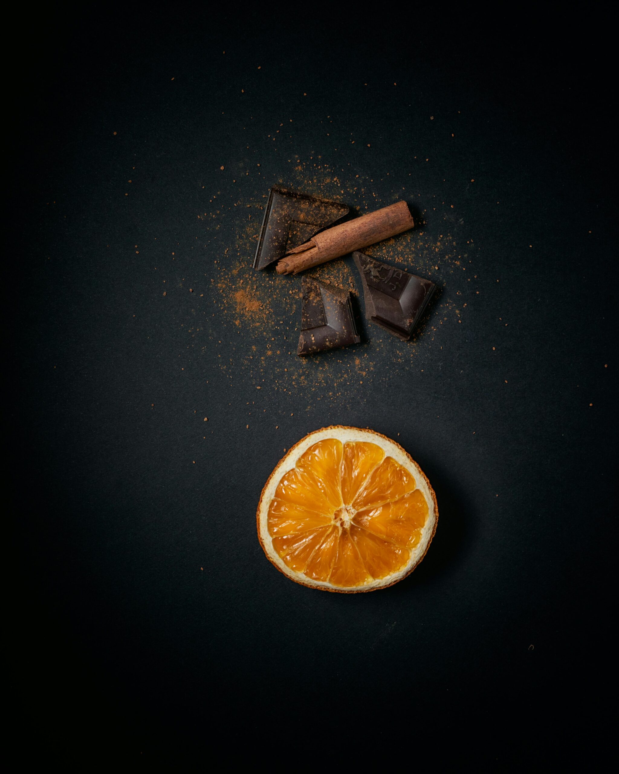 citrus A stylish flat lay of sliced orange, chocolate, and cinnamon sticks on a dark surface.